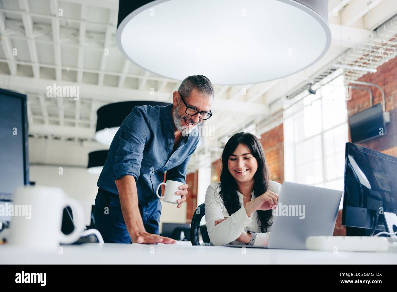 Creative businesspeople making success in the office. Happy mature businessman collaborating with his female colleague in a modern workplace. Two coll Stock Photo