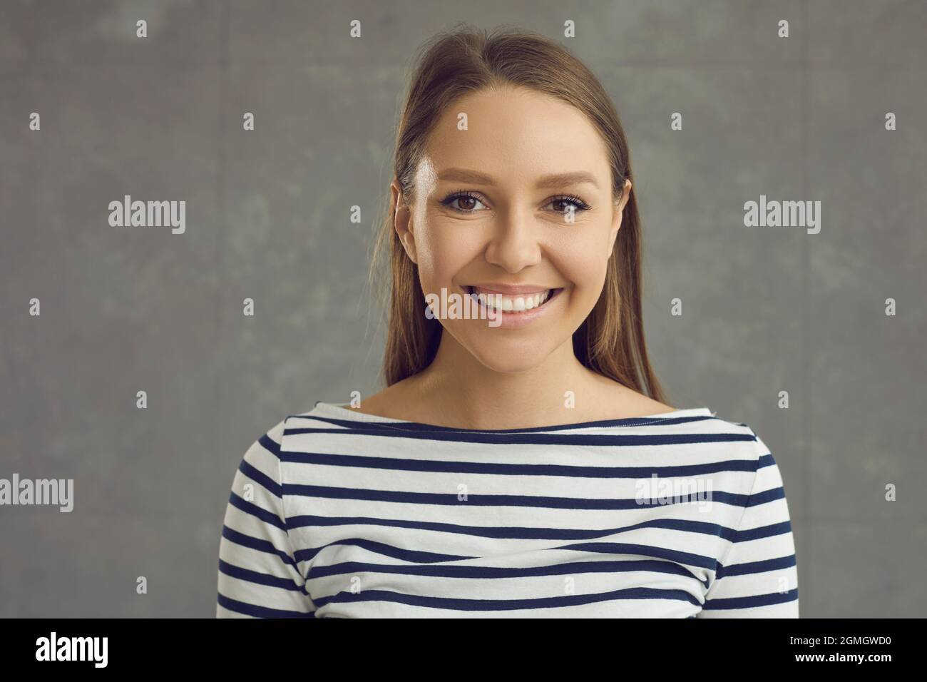 Headshot portrait of young toothy smiling woman on grey studio background Stock Photo