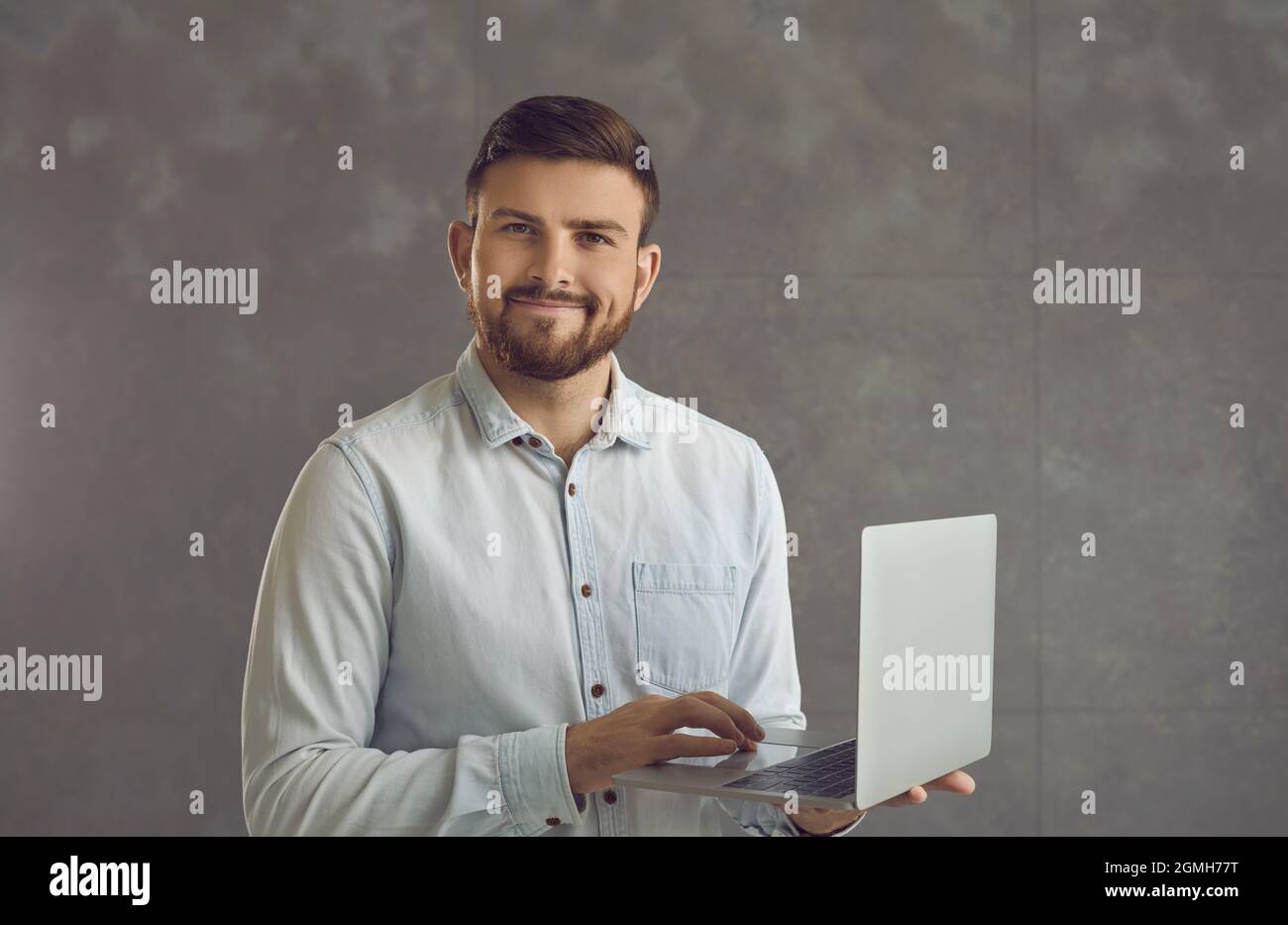Confident smiling business expert man holding laptop standing on studio wall Stock Photo