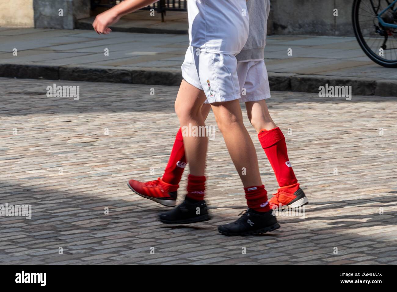 Two school boys walking down a cobbled street in sportswear - close-up of their legs wearing red football socks and white shorts Stock Photo