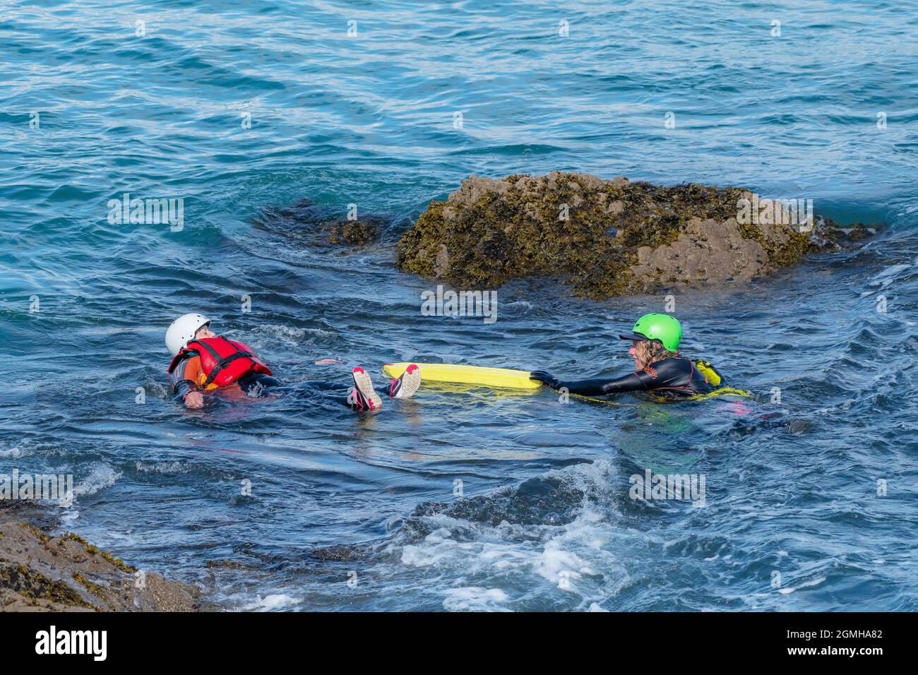 A coasteering guide using a flotation aid to assist a holidaymaker floating in the sea on the coast of Towan Head in Newquay in Cornwall. Stock Photo