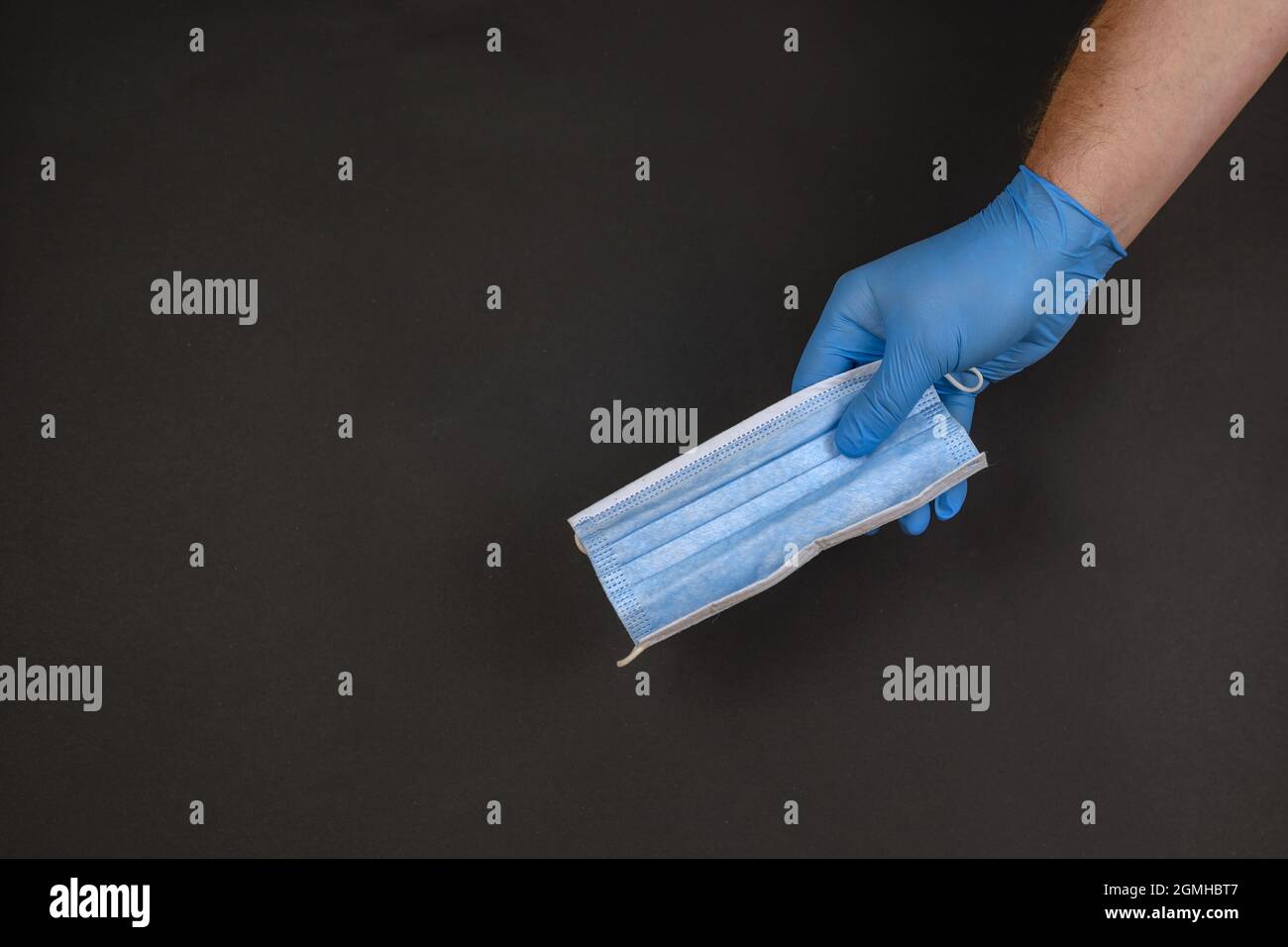 Hand in blue glove holds medical mask. Hand of surgeon against b Stock Photo