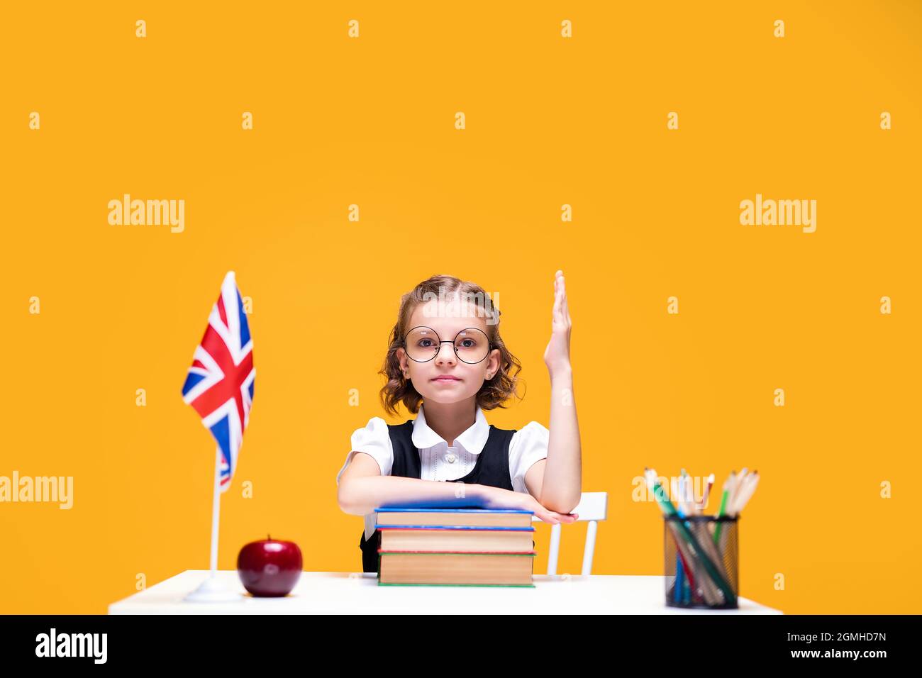 Serious caucasian schoolgirl sitting at the desk and raising hand ...
