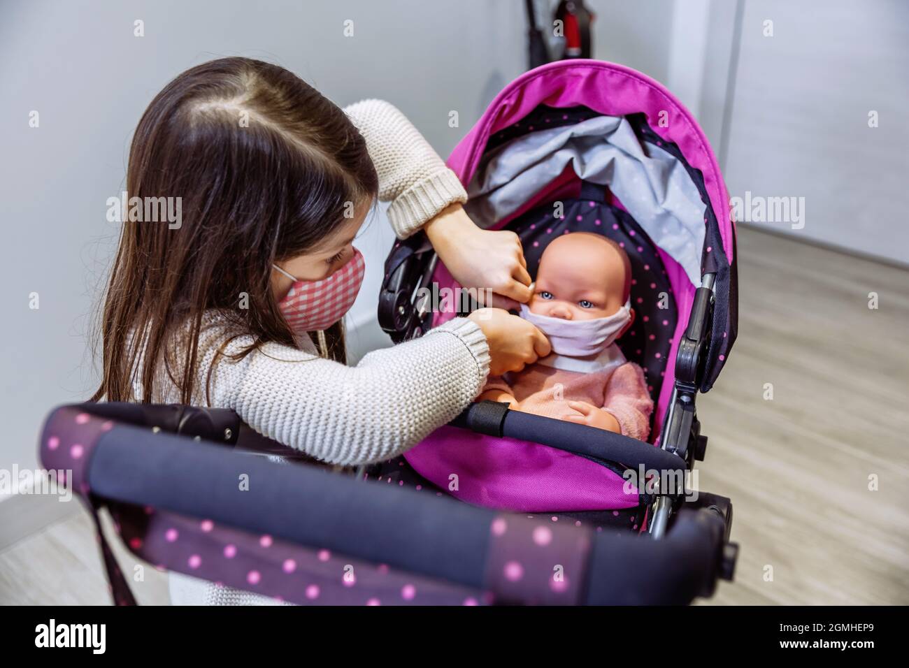 Girl with face mask putting mask on her baby doll Stock Photo
