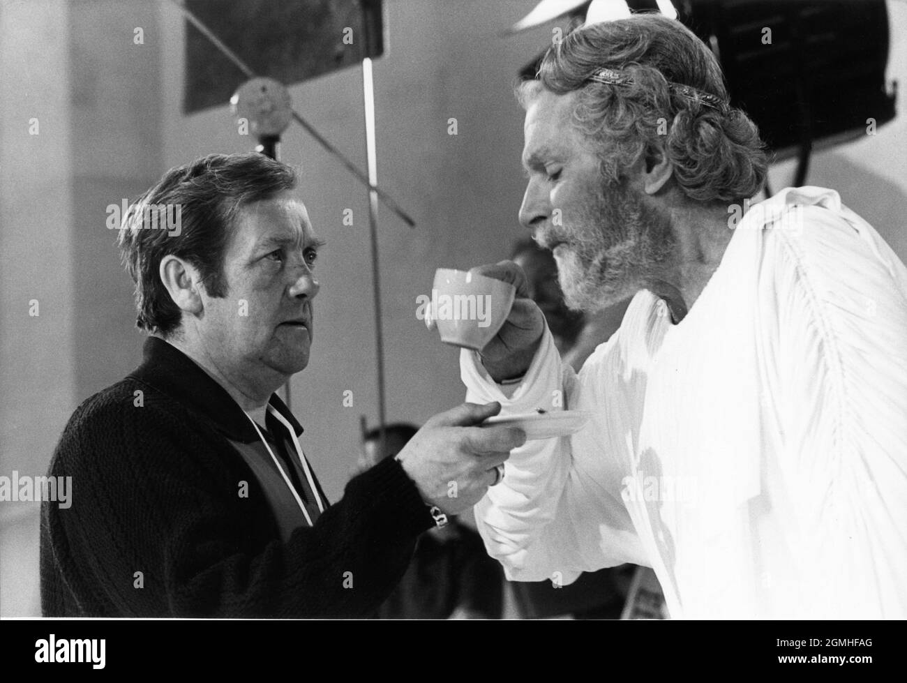LAURENCE OLIVIER in costume as Zeus drinks a cup of tea assisted by a Crew Member on set candid during filming of CLASH OF THE TITANS 1981 director DESMOND DAVIS written by Beverley Cross costume design Emma Porteous creator of special visual effects (Dynamation) Ray Harryhausen music Laurence Rosenthal producers Charles H. Schneer and Ray Harryhausen Charles H. Schneer Productions / Peerford Ltd. / distribution Cinema International Corporation (CIC)  (UK) Metro Goldwyn Mayer (USA) Stock Photo