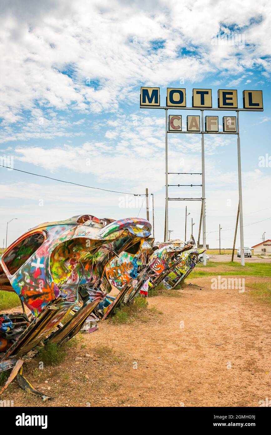 painted Volkswagen Beetles half buried at an angle at Slug Bug Ranch Amarillo Texas on Route 66 with old motel and cafe sign Stock Photo