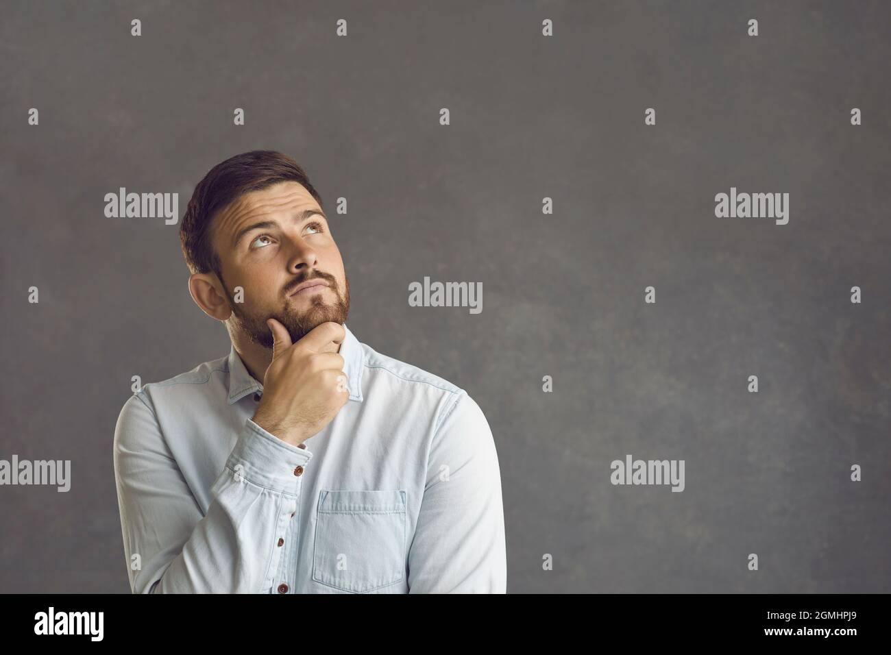 Pensive thoughtful caucasian bearded man touching chin looks up studio shot Stock Photo