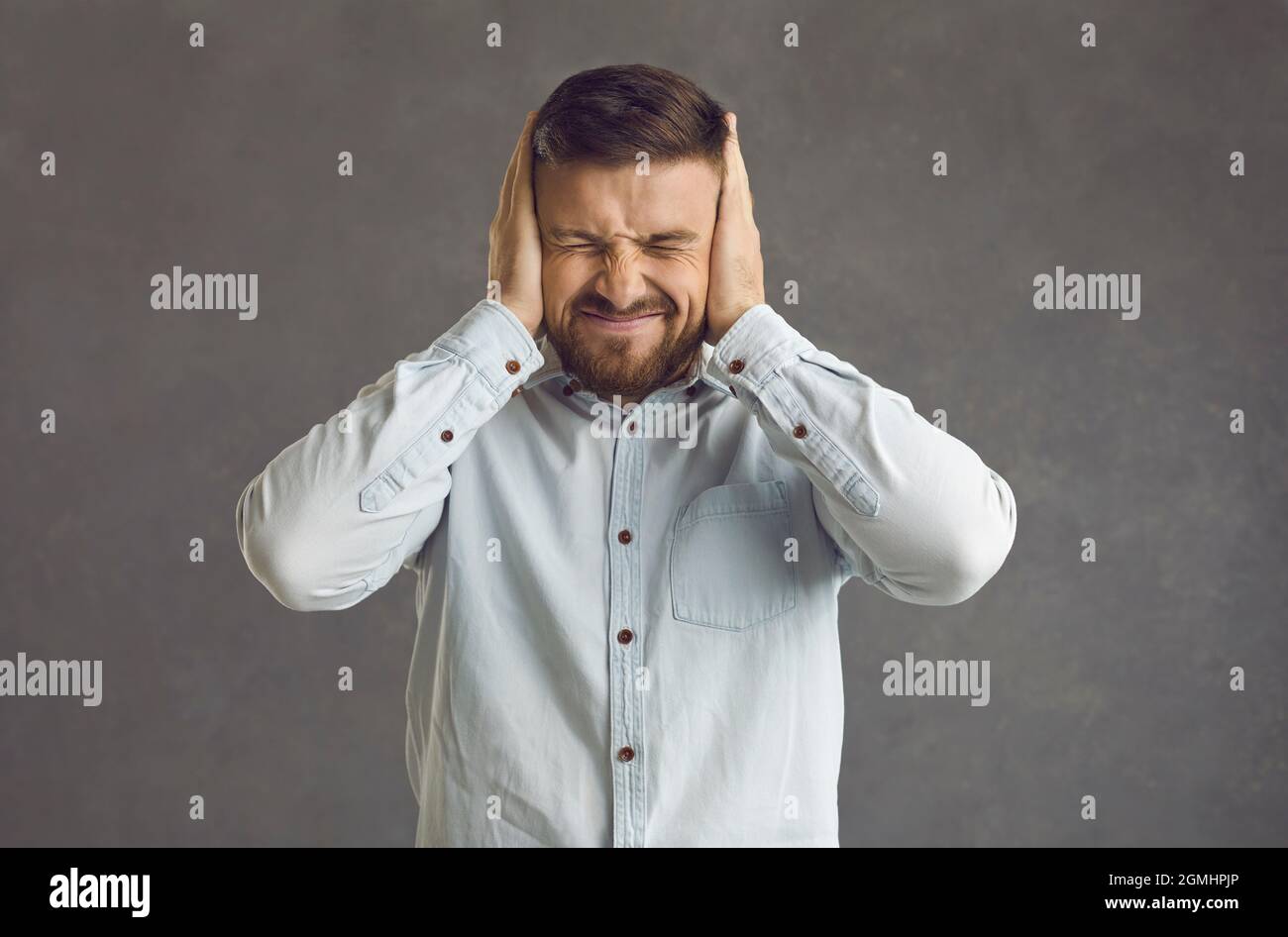 Stressed frustrated man with closed eyes and covered ears by hands squints Stock Photo