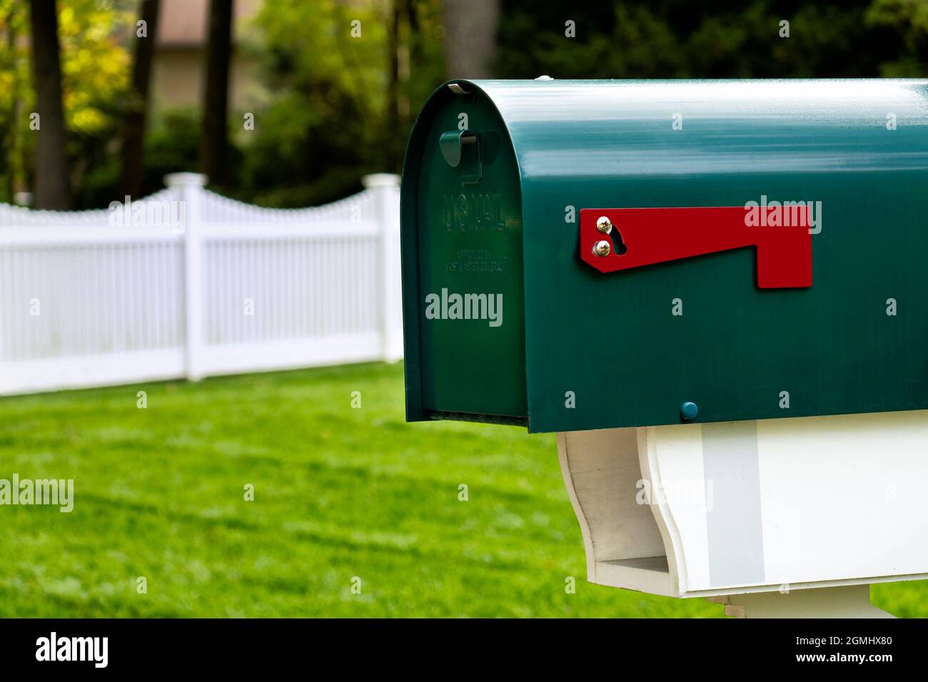 Green mailbox and newspaper slot with scalloped picket fence in background. Stock Photo