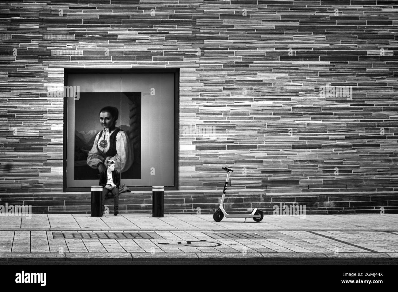 Oslo, Norway. September 2021.  a boy sitting waiting with a reproduction of a painting behind him on a perimeter wall of the National Art Museum in th Stock Photo