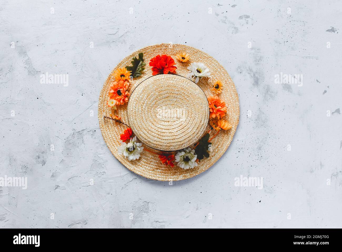 Grey concrete flat lay background with colorful autumn flower heads on straw hat Stock Photo