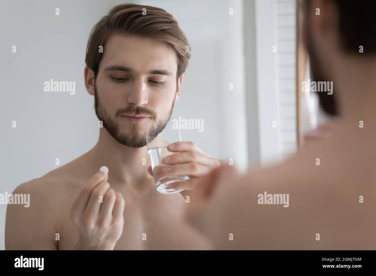 Guy taking supplement holding glass of water and pill Stock Photo
