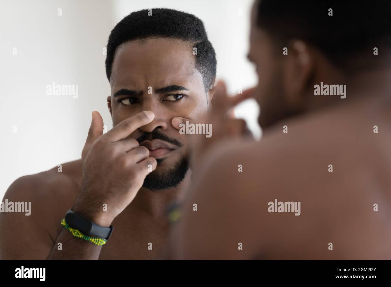 African guy looks in mirror touch face squeezes pimple Stock Photo