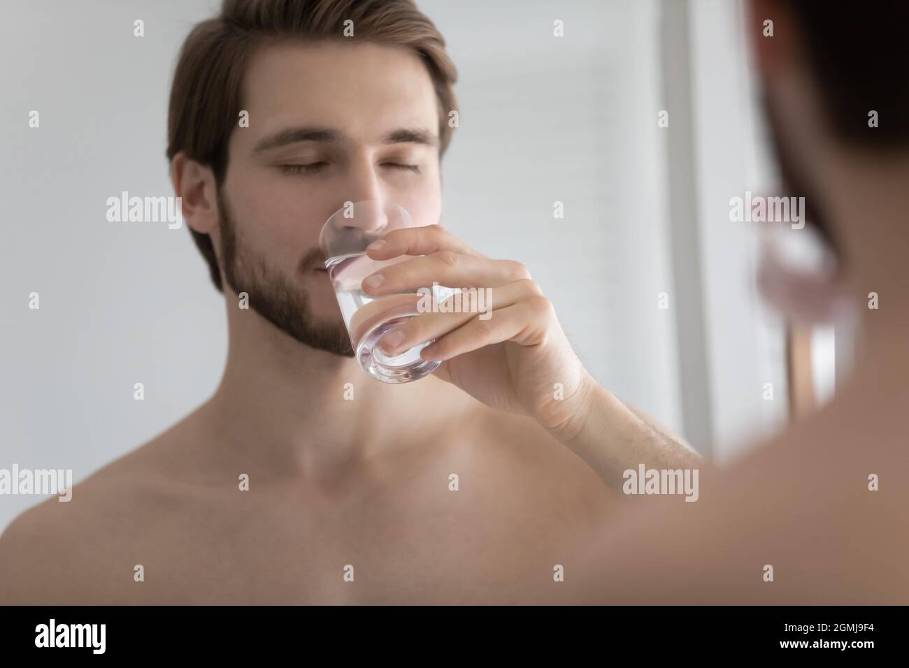 Man reflecting in mirror while drinks clean still mineral water Stock Photo