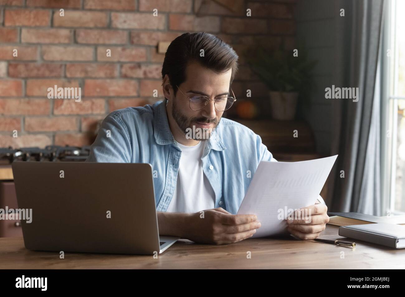 Confident businessman in glasses reading document, sitting at table Stock Photo
