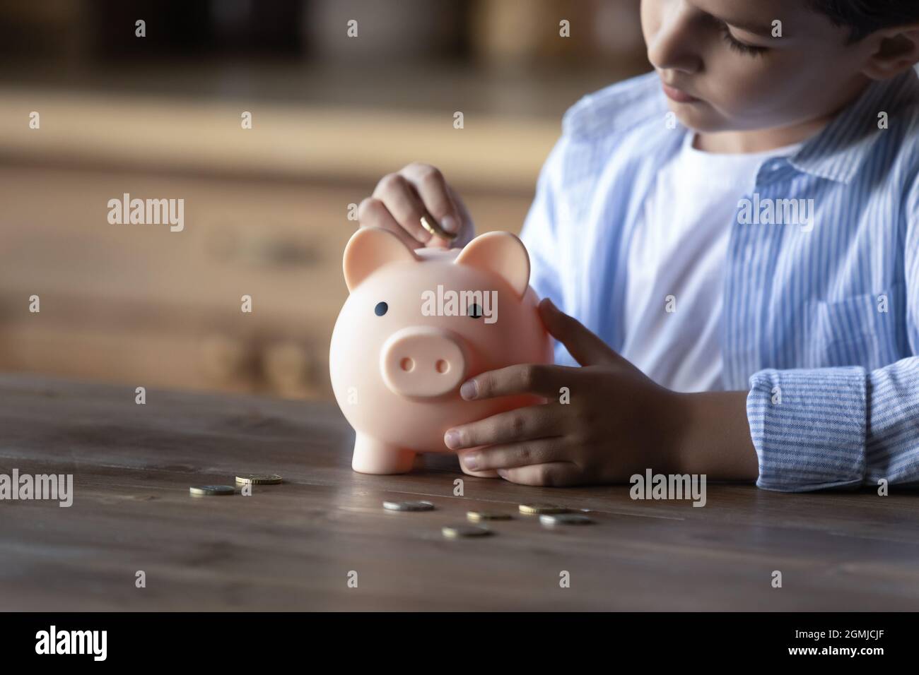 Crop close up 8s boy putting coin into piggy bank Stock Photo - Alamy
