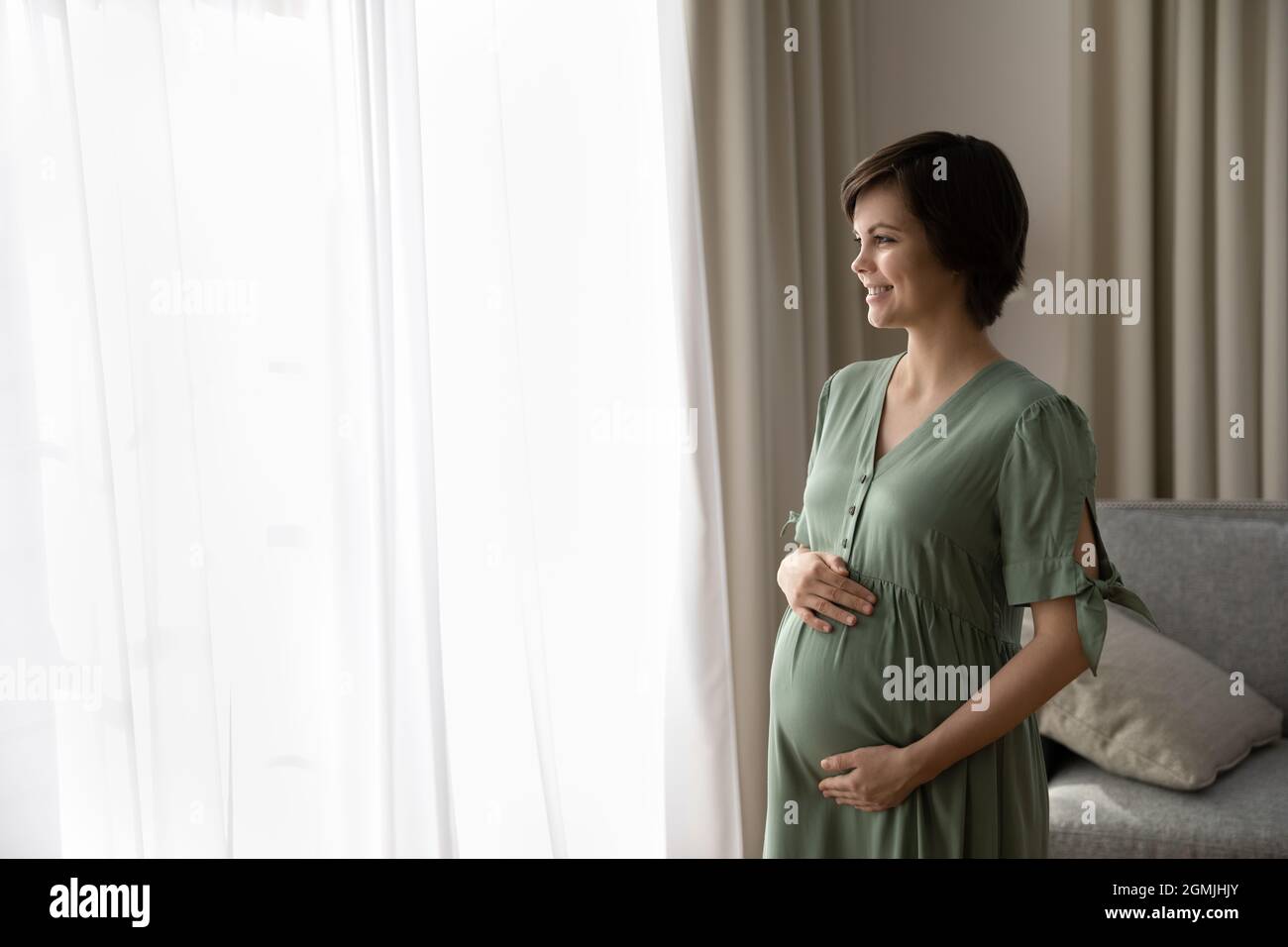Hopeful future mom touch belly look in light window Stock Photo