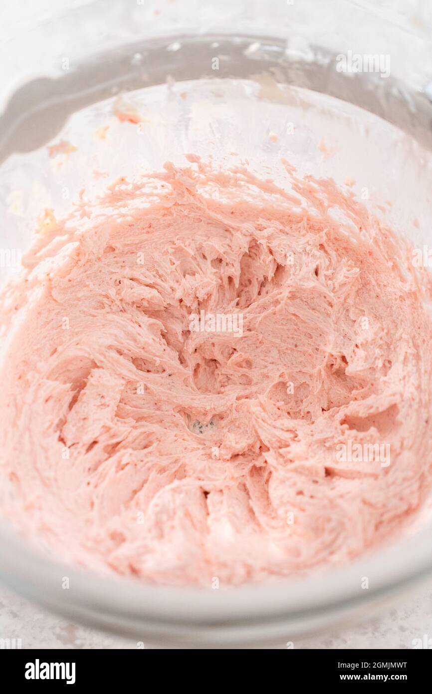 Whipping strawberry buttercream frosting in a standalone electric mixer with a whisk attachment