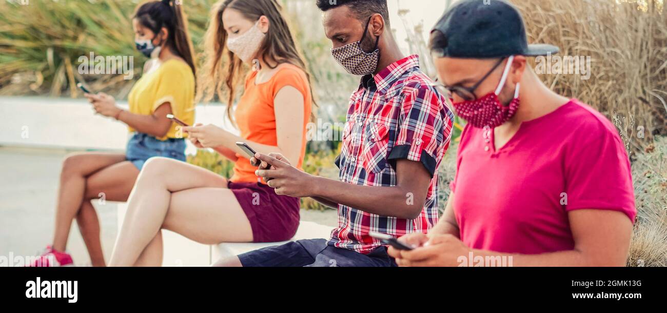 Friends using their smartphones in covid 19 times protected with face mask - Young people using mobile device in distance outdoors Stock Photo