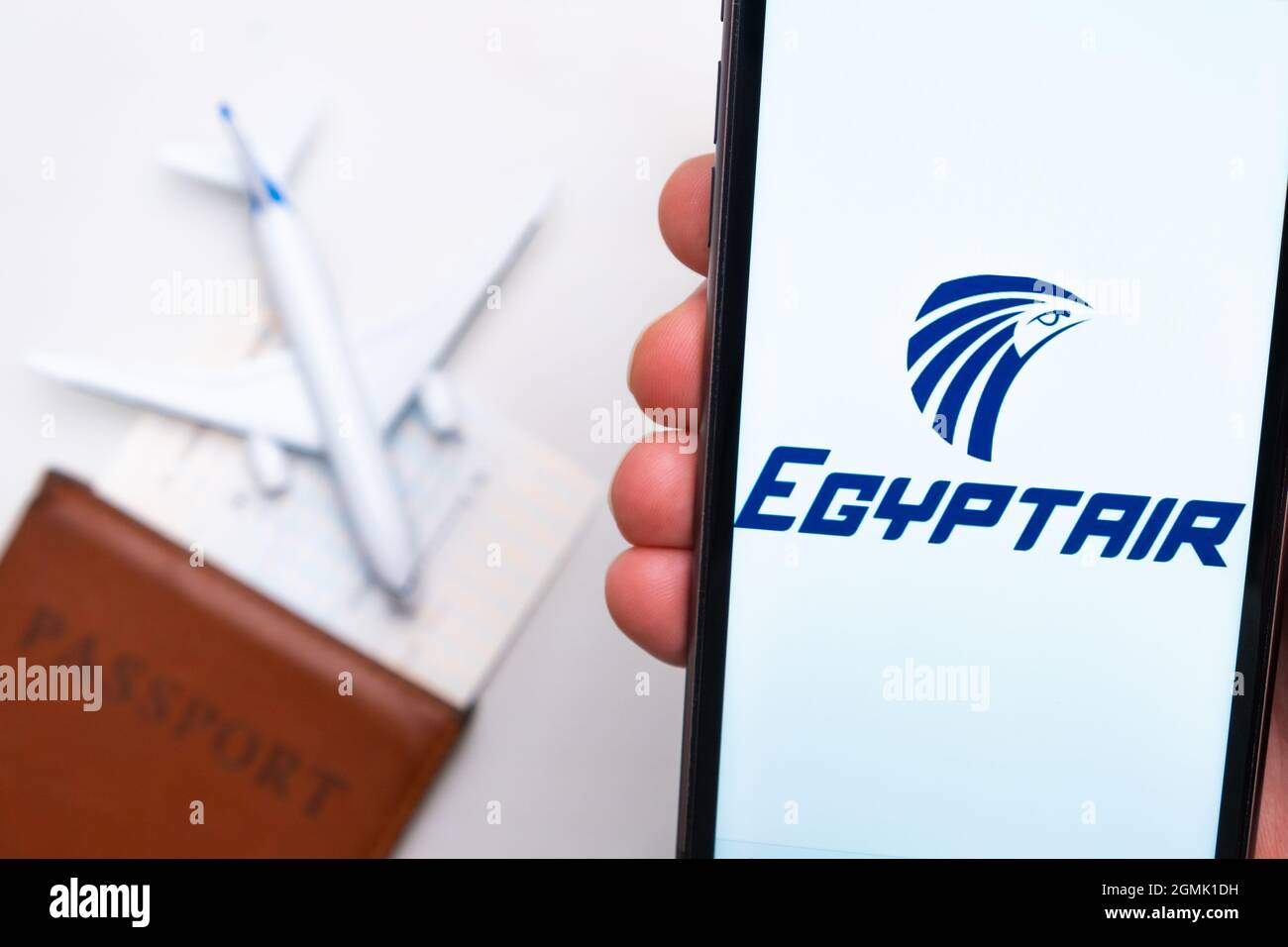EgyptAir airline company logo on the screen of mobile phone in man hand on the background of passport, boarding pass and plane, September 2021, San Stock Photo