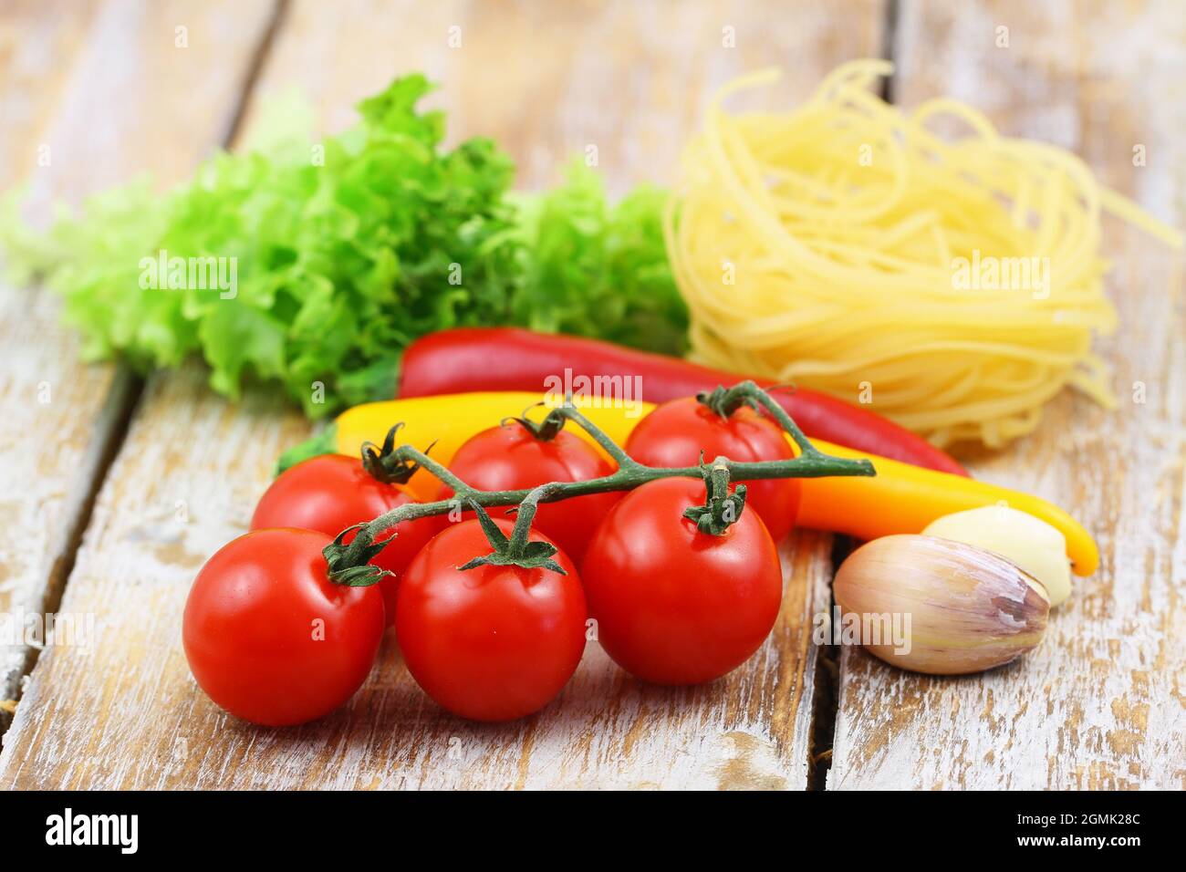 Selection of cooking ingredients: tagliatelle, cherry tomatoes, garlic cloves and chilies on woodenrustic surface Stock Photo