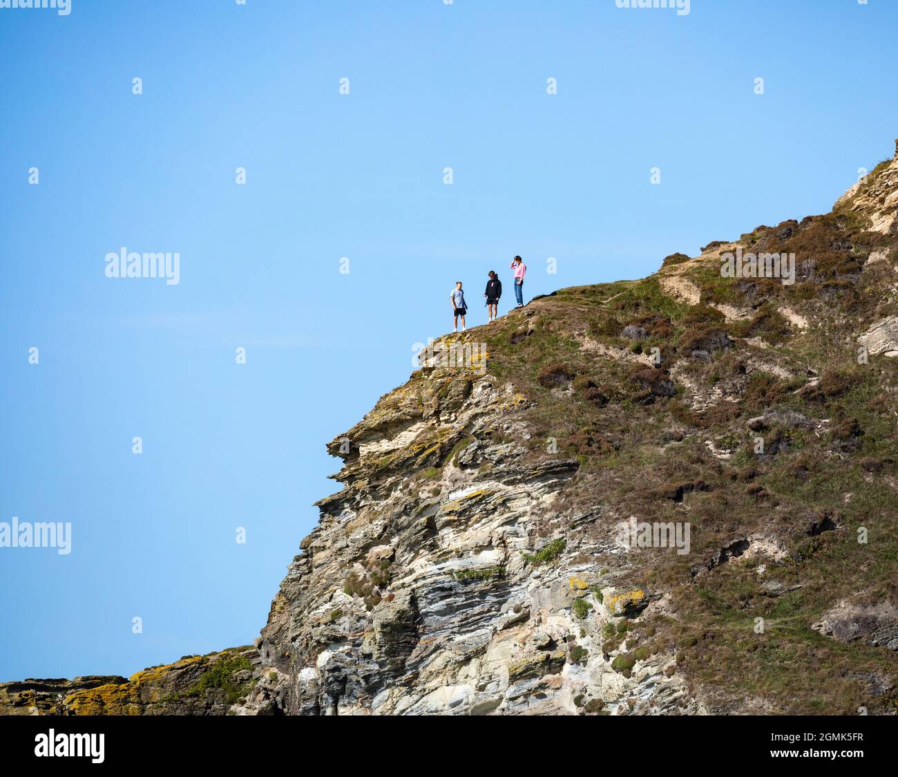 Three people standing on a cliff edge in Portreath, Cornwall, UK Stock Photo