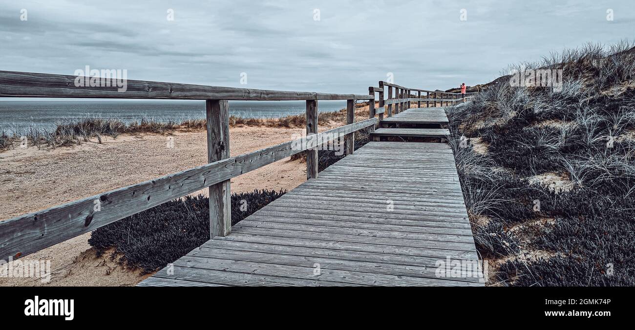 A wooden boardwalk on an elevated grassy coast under a cloudy sky Stock ...