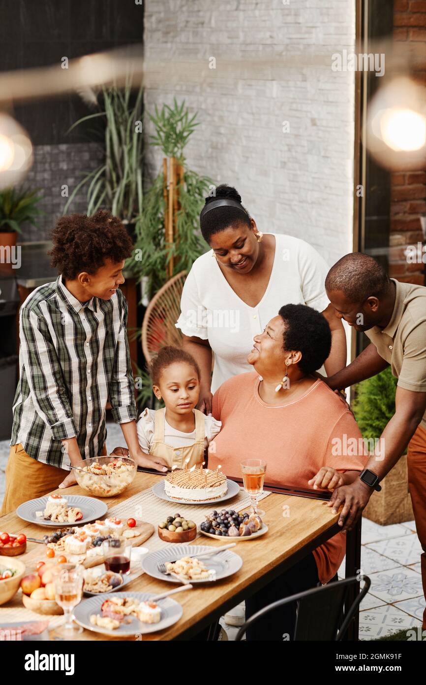 Vertical portrait of senior African-American woman celebrating birthday with family and blowing candles on Birthday cake Stock Photo