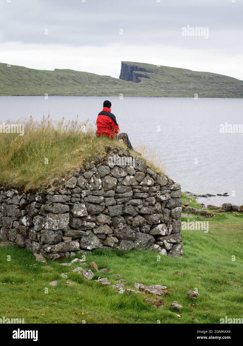 View of Lake Leitisvatn or Sorvagsvatn on Vagar Island, Faroe Islands. A tourist in a red jacket enjoys the beautiful northern nature Stock Photo