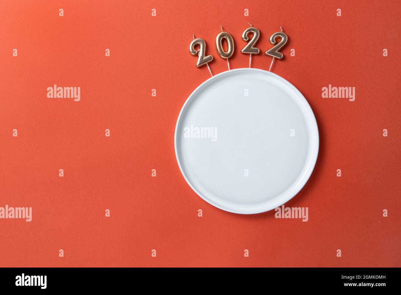 Creative Christmas table setting. Empty plate with straight edges, candles in form of numbers 2022, on red background, copy space, minimal layout, moc Stock Photo