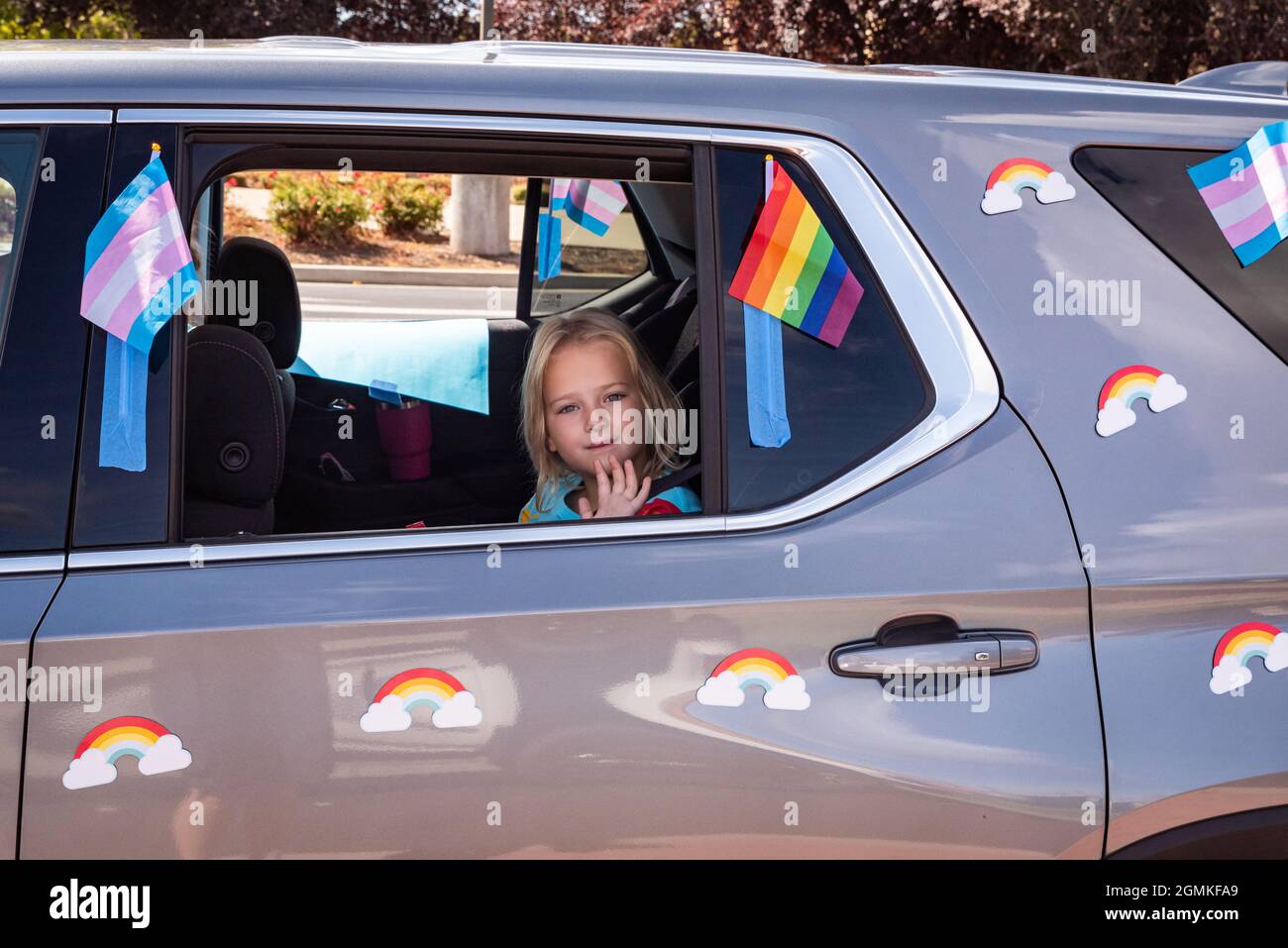 ROSEVILLE, CA, U.S.A. - SEPT. 19, 2021: A small child waves out a window of a car decorated with rainbow and transgender flags as part of Placer Count Stock Photo
