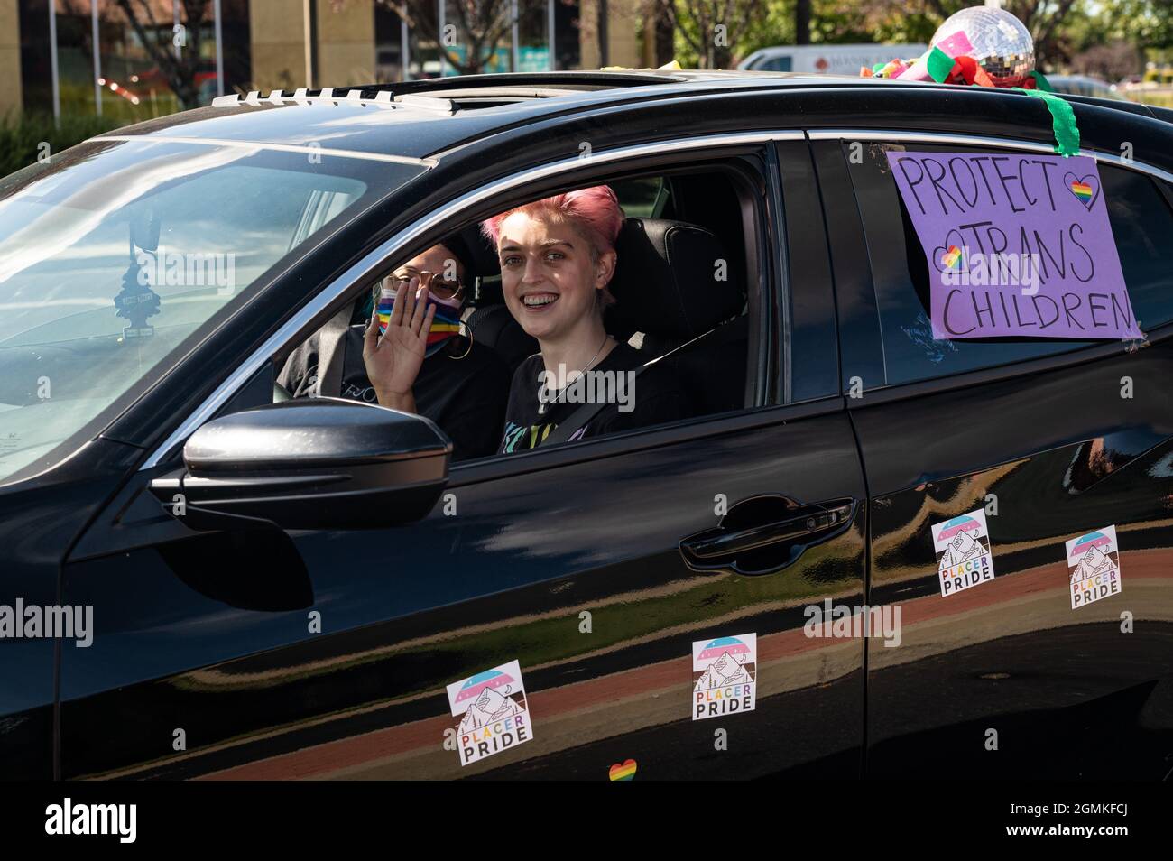 ROSEVILLE, CA, U.S.A. - SEPT. 19, 2021: A young person with pink hair smiles and a person in a rainbow mask waves while driving a 'Protect Trans Child Stock Photo