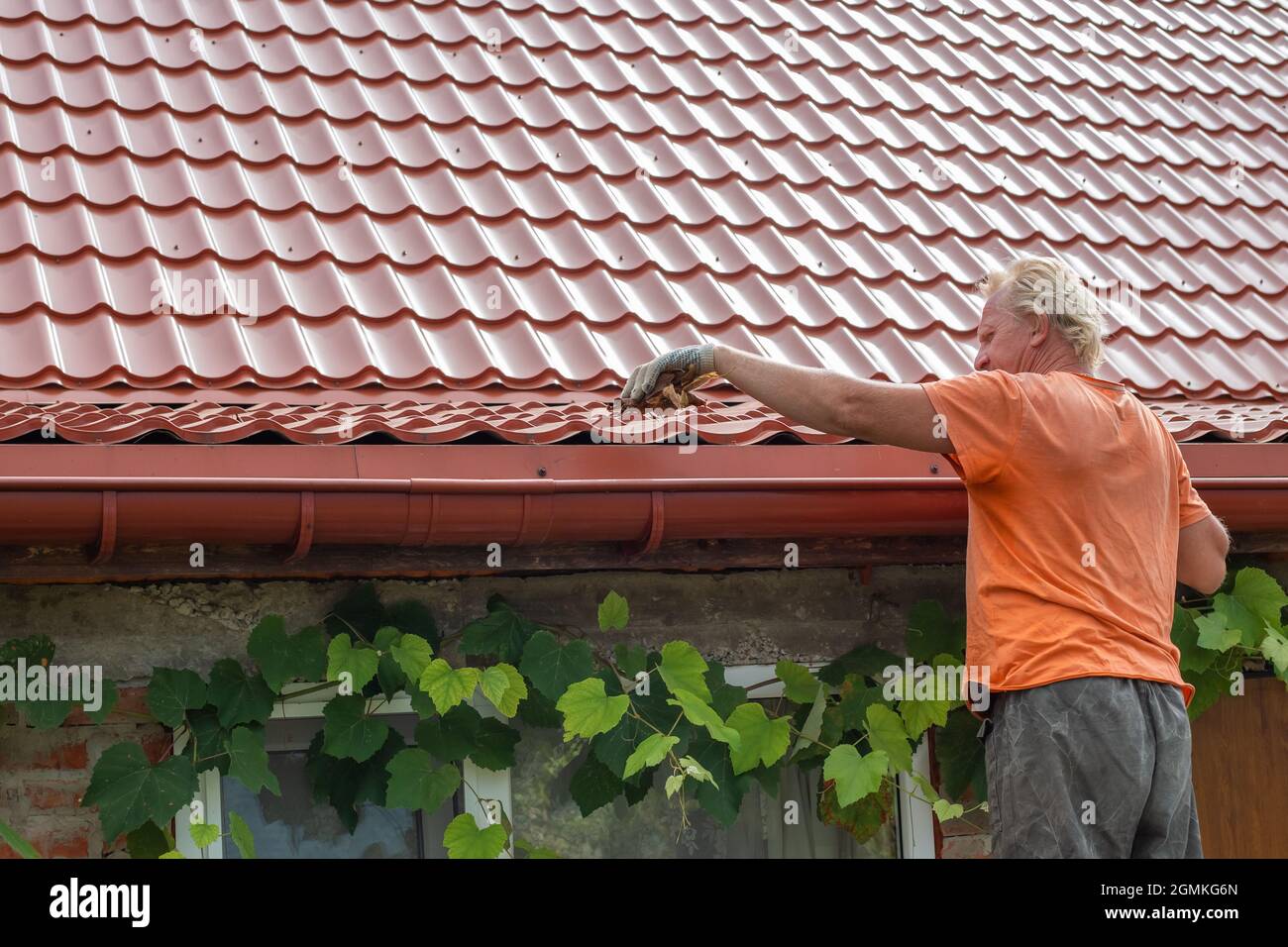 A man cleans out debris and leaves from the gutter system on the roof ...