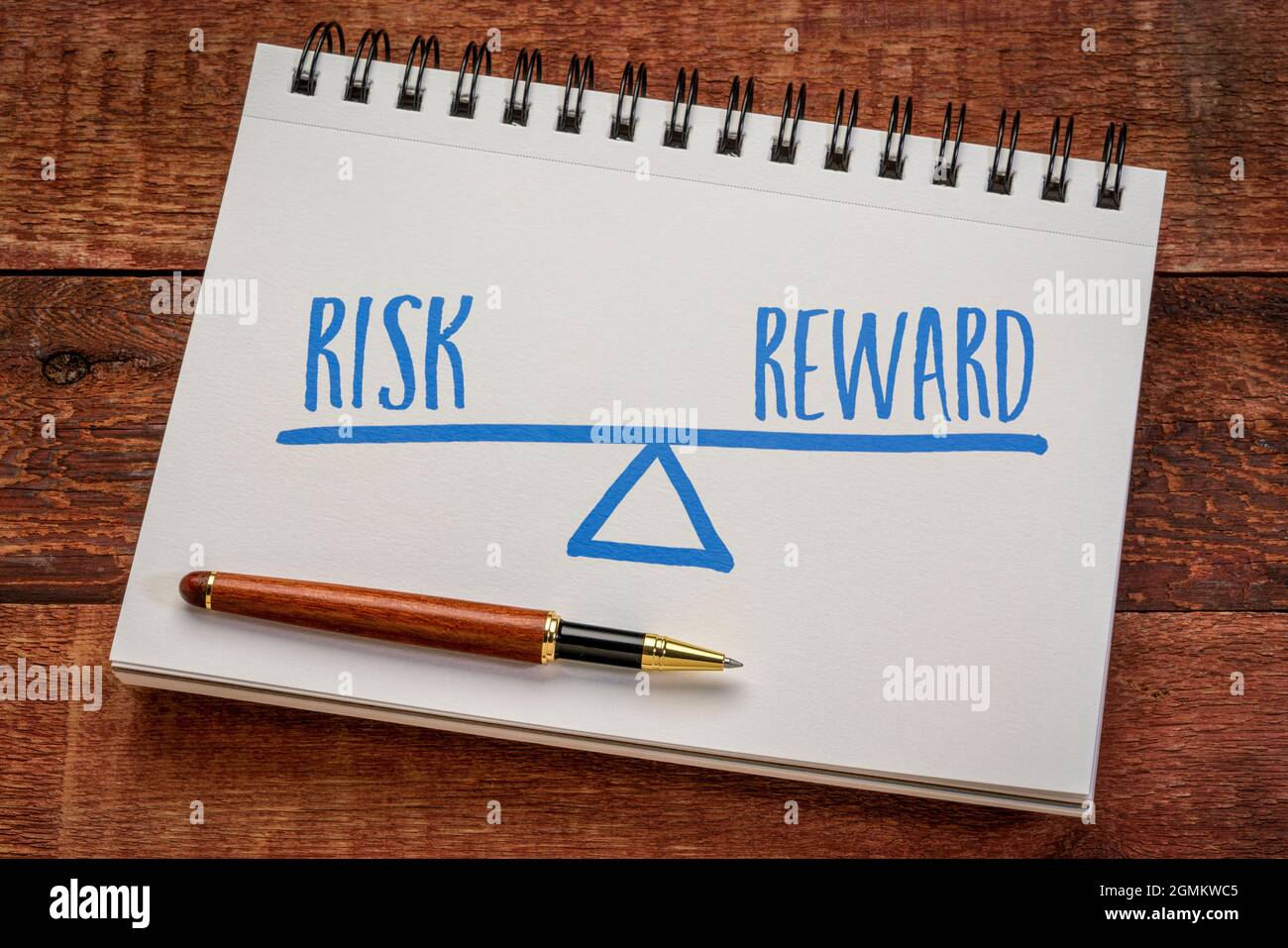 risk and reward balance concept, sketch in a spiral notebook with a stylish pen against weathered barn wood table Stock Photo