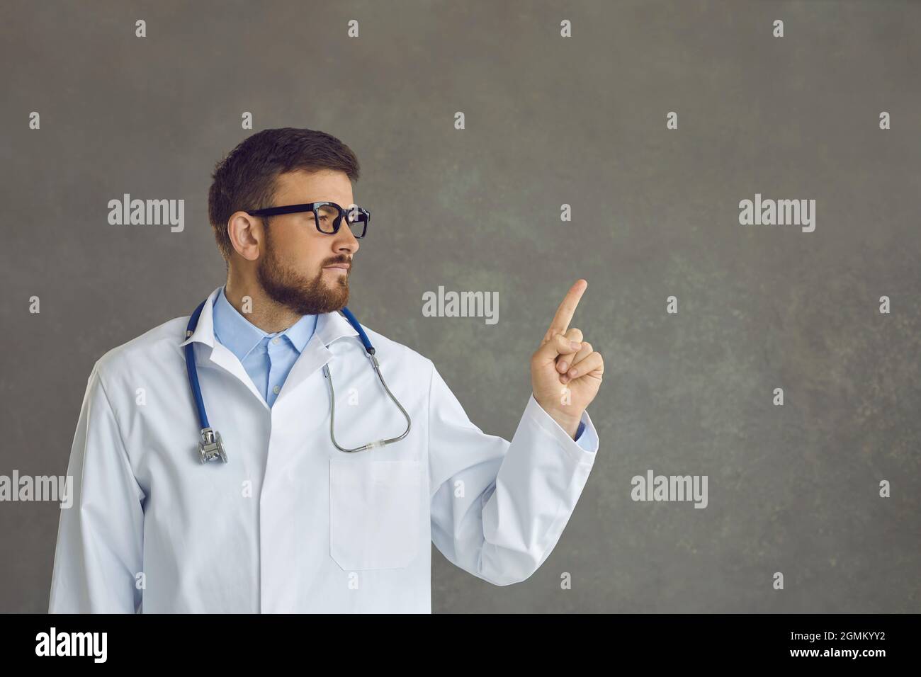 Handsome young doctor isolated on gray background points finger at copy space for text Stock Photo