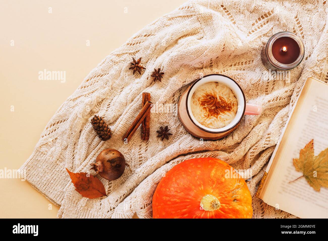 A cup of pumpkin latte on the table with book, candle, yellow leaves and spices on a knitted sweater background. Autumn concept, top view, flat lay Stock Photo