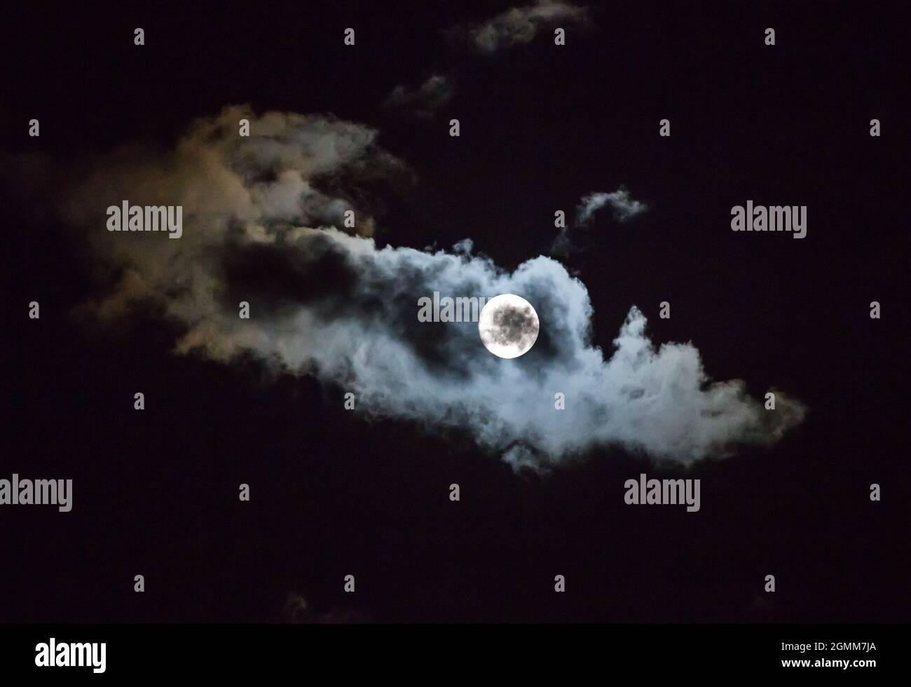 A full moon illuminates passing clouds in a night sky. Stock Photo