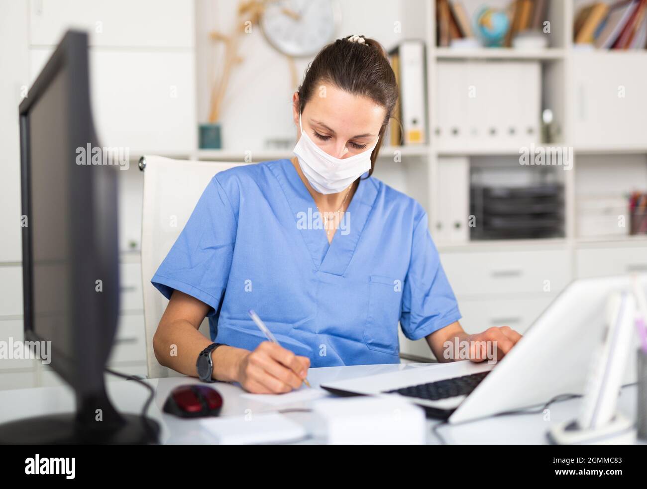 Young Woman Doctor In A Protective Mask Writes Important Notes While Sitting At A Work Desk In Front Of A Computer Stock Photo Alamy