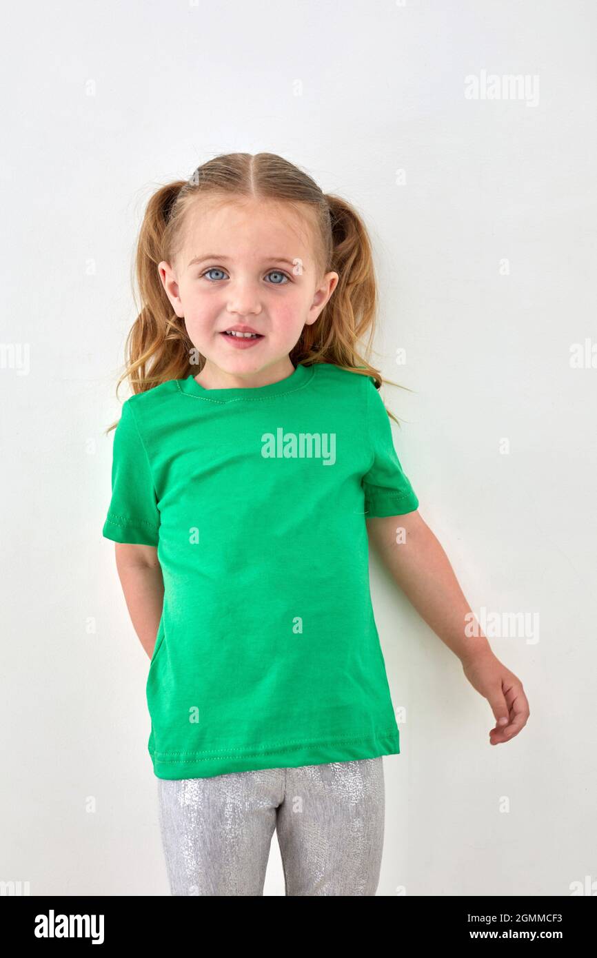 Adorable toddler girl with ponytails dressed in bright green t shirt looking at camera and smiling against white background Stock Photo