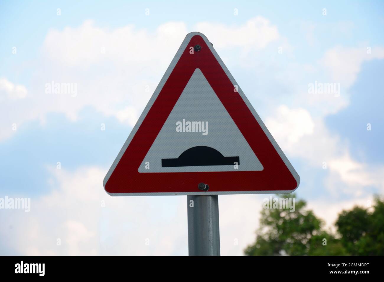 Speed bump sign. Triangle traffic sign warning there is a threshold coming up in the road. Symbol against a blue sky with clouds and trees. Signs givi Stock Photo