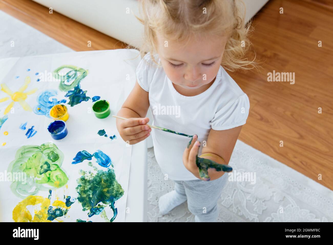 Toddler girl painting at home. Happy creative child spending time with fun and joy. Learning colours Stock Photo