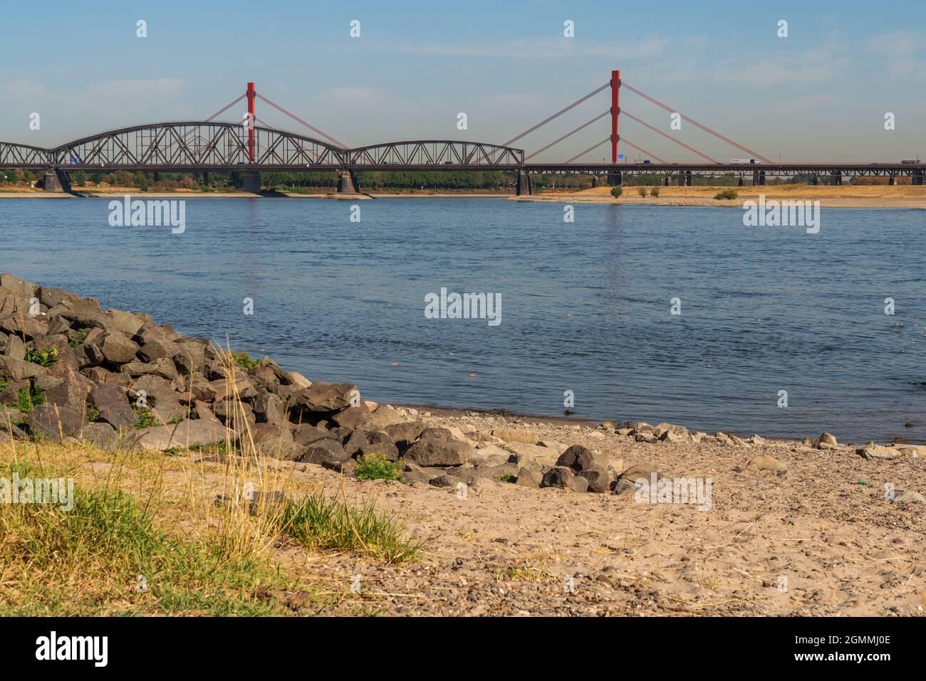 Duisburg, North Rhine-Westfalia, Germany - August 07, 2018: A parched meadow at the River Rhine with the Beeckerwerther Bridge and the Haus-Knipp Rail Stock Photo