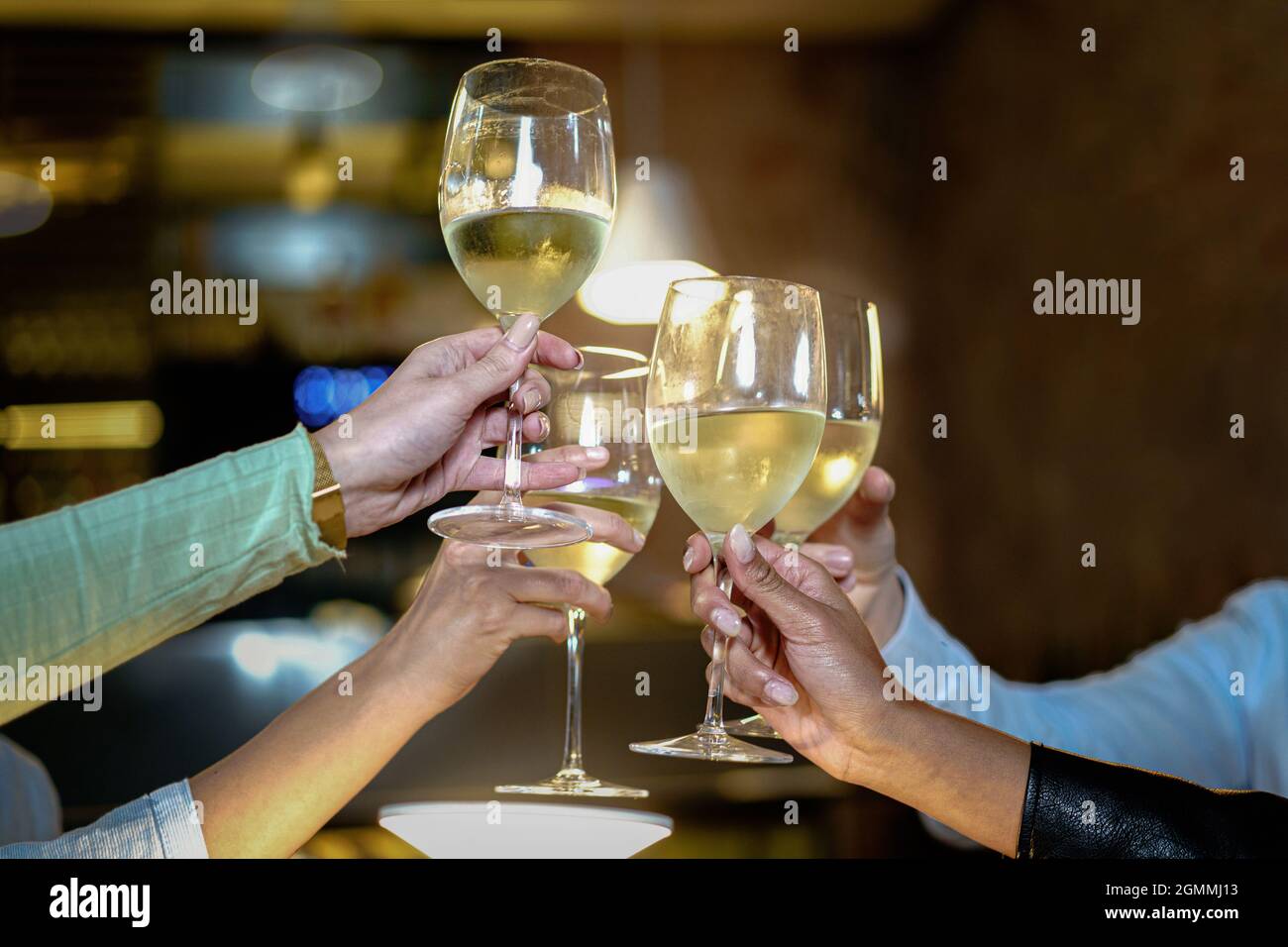 Toast at the restaurant. Detail on the clinkering white wine glasses. Concept of friends having a toast together by raising their wineglasses. Stock Photo