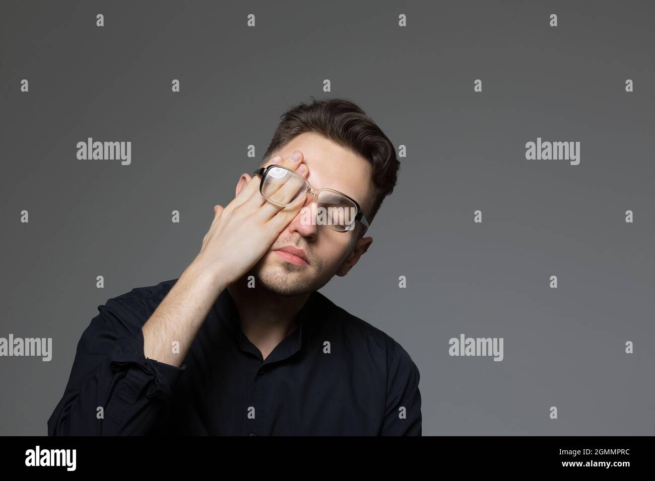 Tired young man rubbing eyes Stock Photo