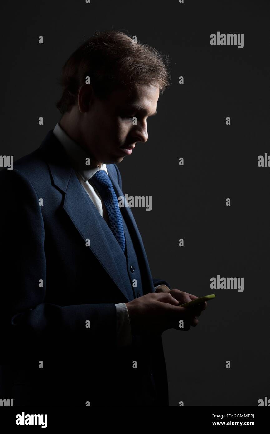 Businessman in suit texting with smart phone on black background Stock Photo