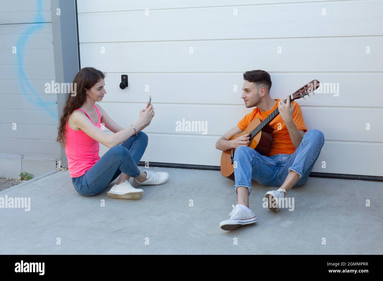 Young woman photographing boyfriend playing guitar in driveway Stock Photo