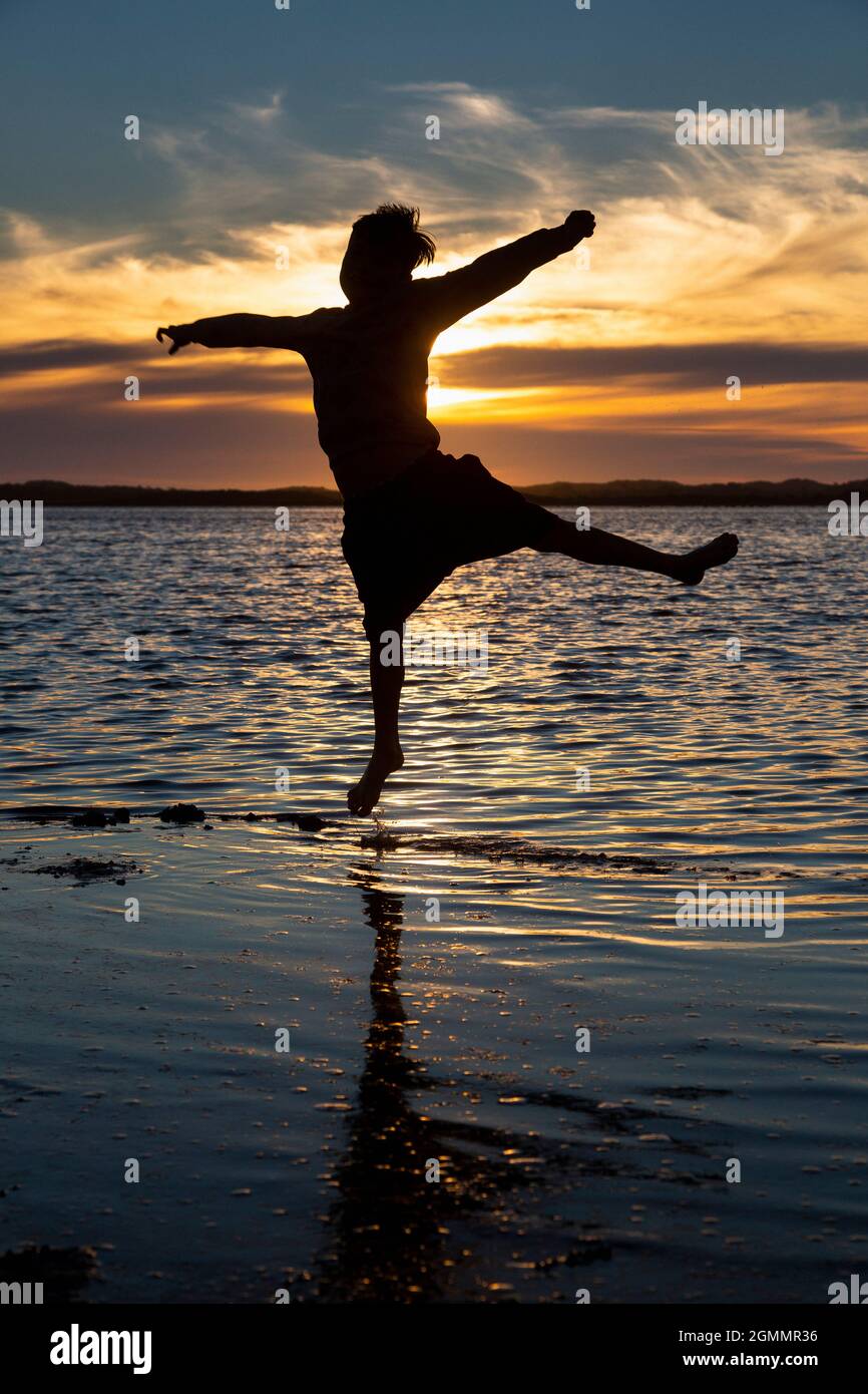 Silhouette boy jumping in ocean surf at sunset Stock Photo