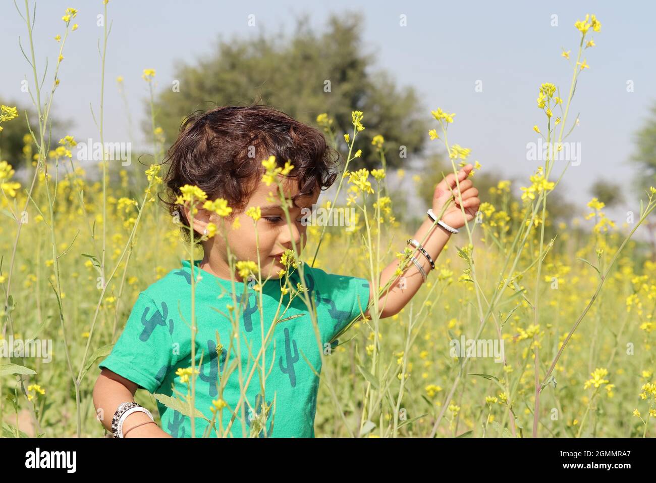 Close-up portrait of A beautiful cute Indian Hindu little child enjoying and playing in a mustard field wearing a green shirt Stock Photo