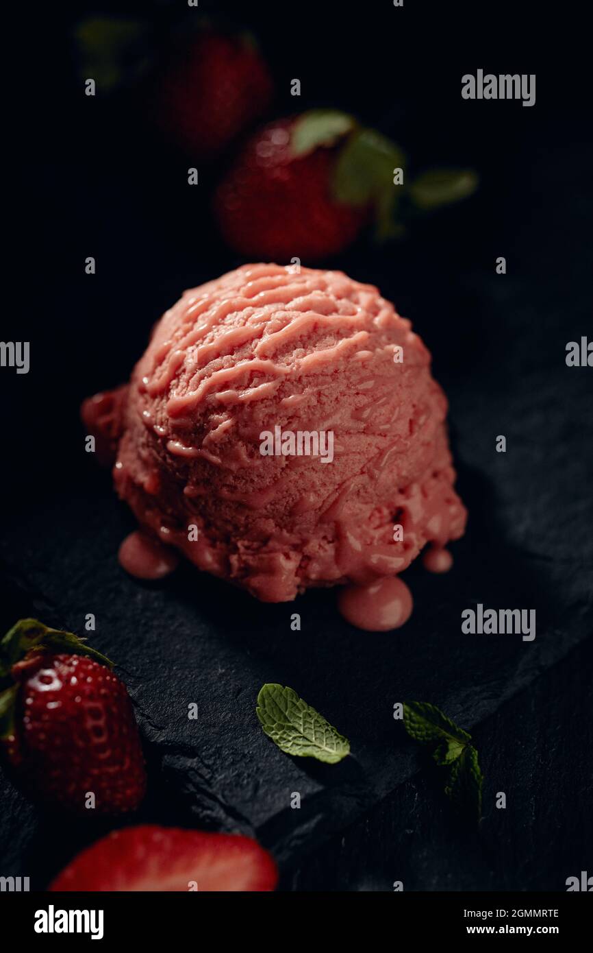 Tasty creamy gelato scoop between ripe strawberries and fresh mint leaf on blurred background Stock Photo