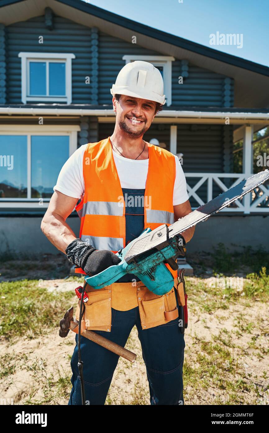 Happy construction worker standing with chainsaw in hands Stock Photo